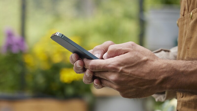 En person håller i en mobil i ett växthus