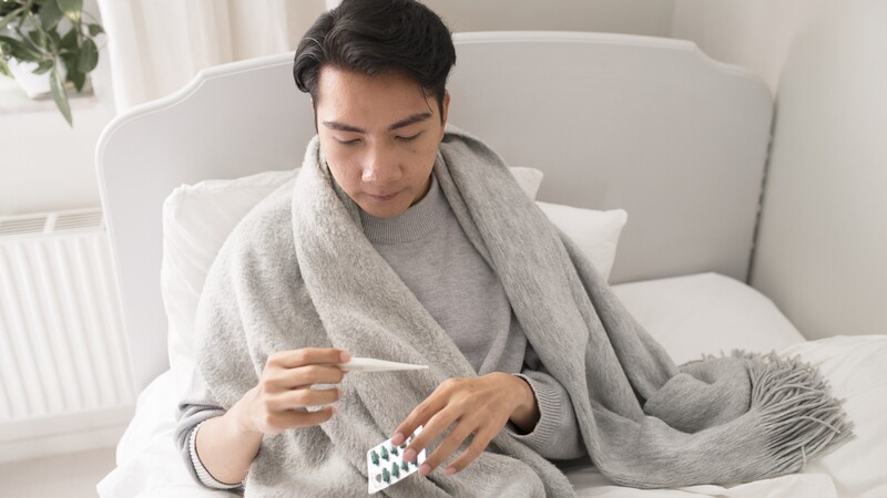 Man in bed looking at thermometer