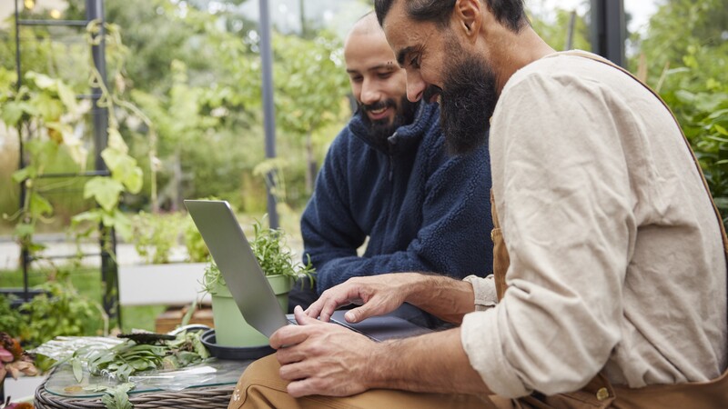 Två personer framför en dator arbetar i en trädgård. 