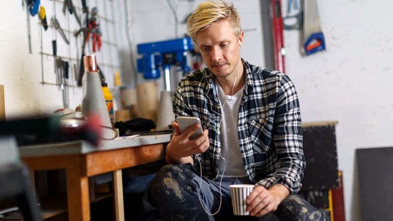 man in checkered shirt looking at mobile phone in workshop