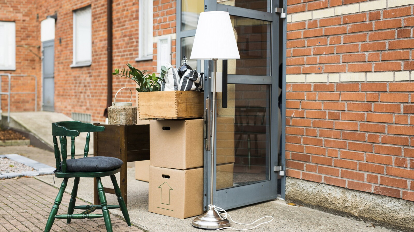 Moving boxes, a chair, and a lamp outside a building.